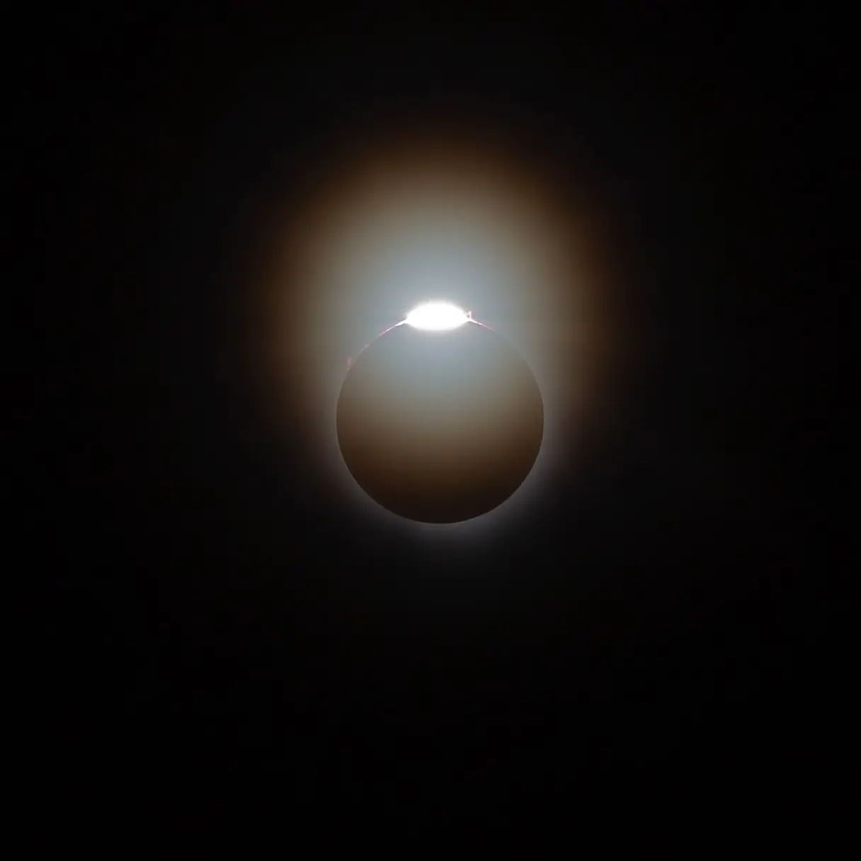 The diamond ring effect at the start of a total solar eclipse, with mild corona and red prominences visible.