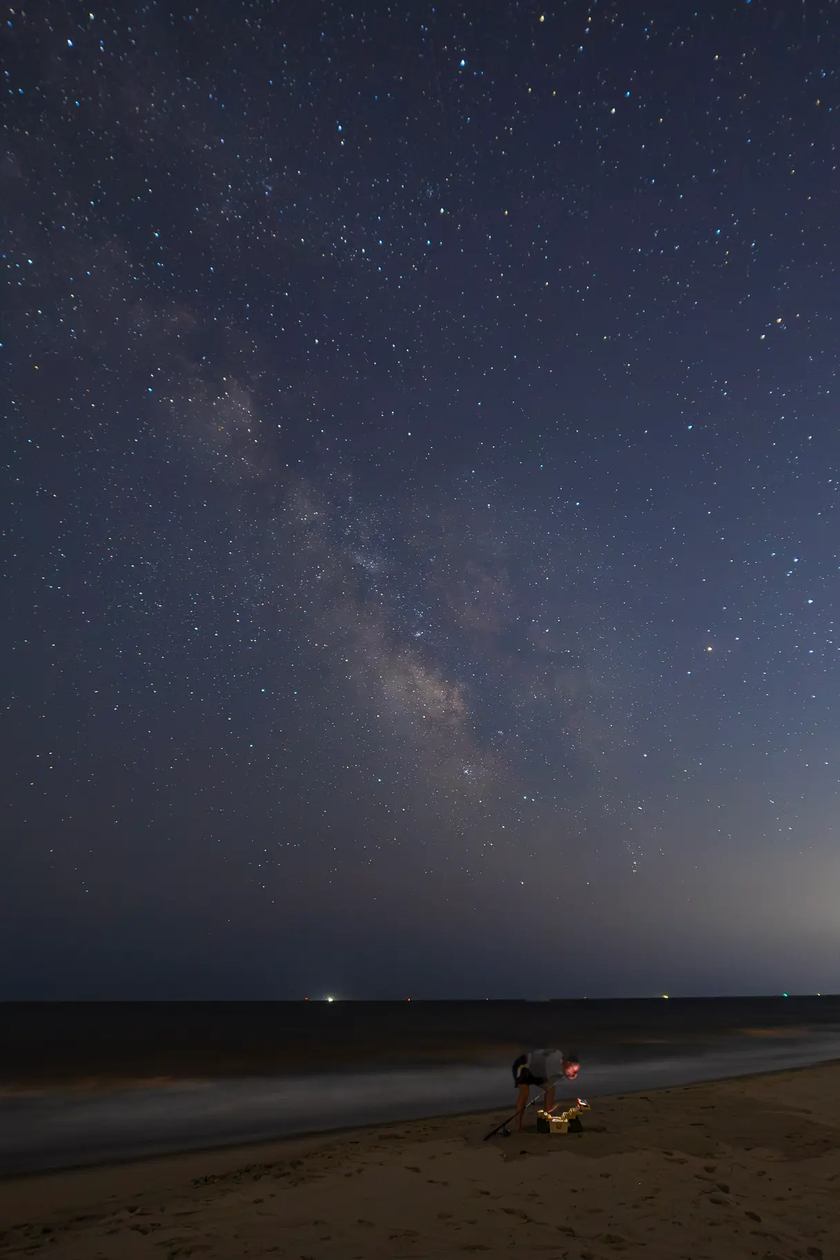The Milky Way core visible over a beach while a fisherman heads back to his tackle box.