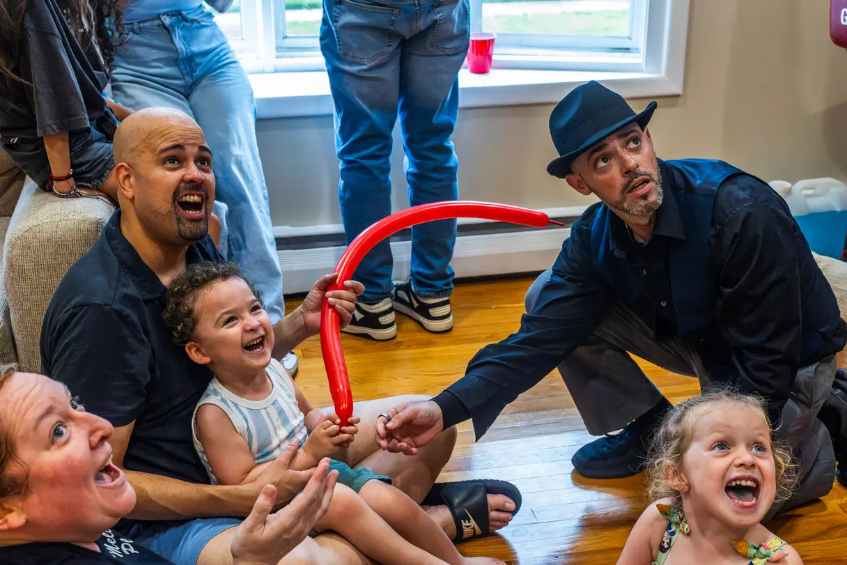 Surprised party guests laughing and watching a magic trick being performed.