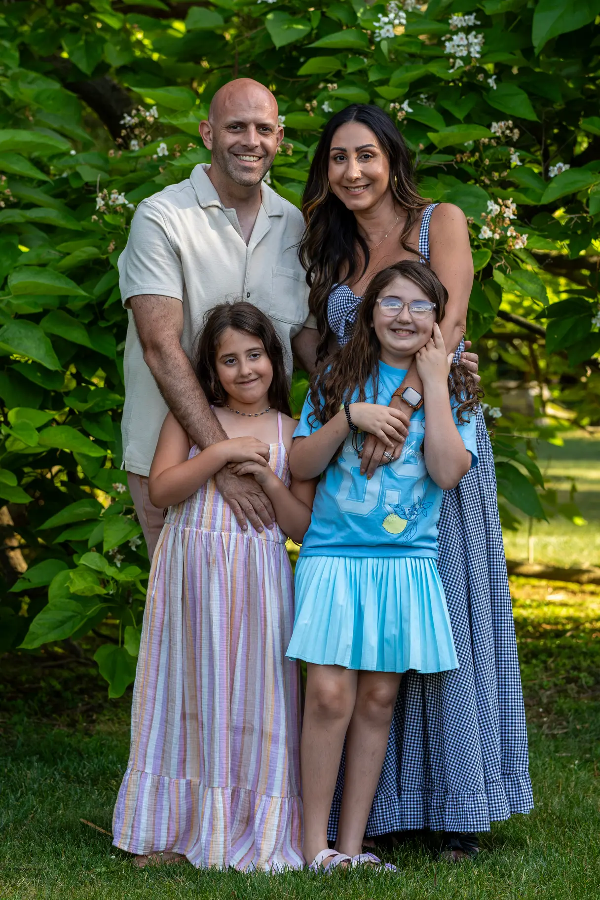 Family of four in a loving embrace against a natural background during golden hour.